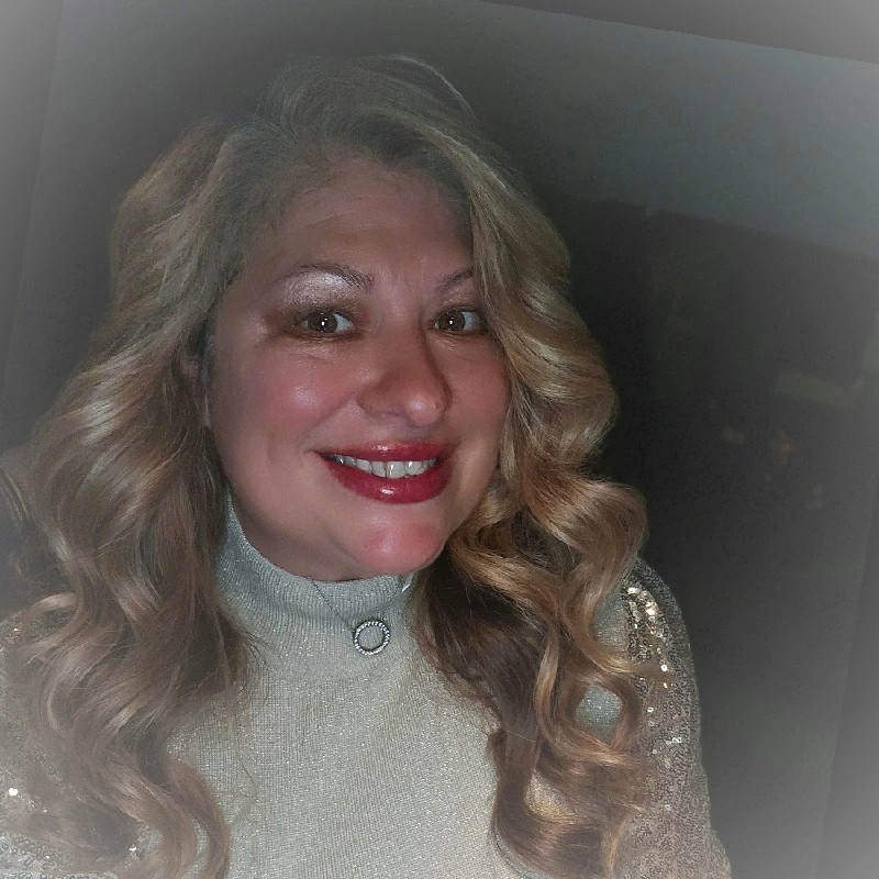 Smiling woman with long wavy blonde hair wearing a sparkly silver top.