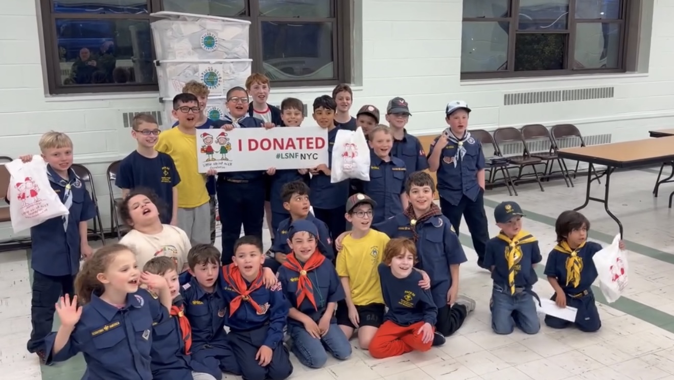 Group of young scouts posing indoors with an 'I DONATED' banner and donation bags after a drive in a gym.
