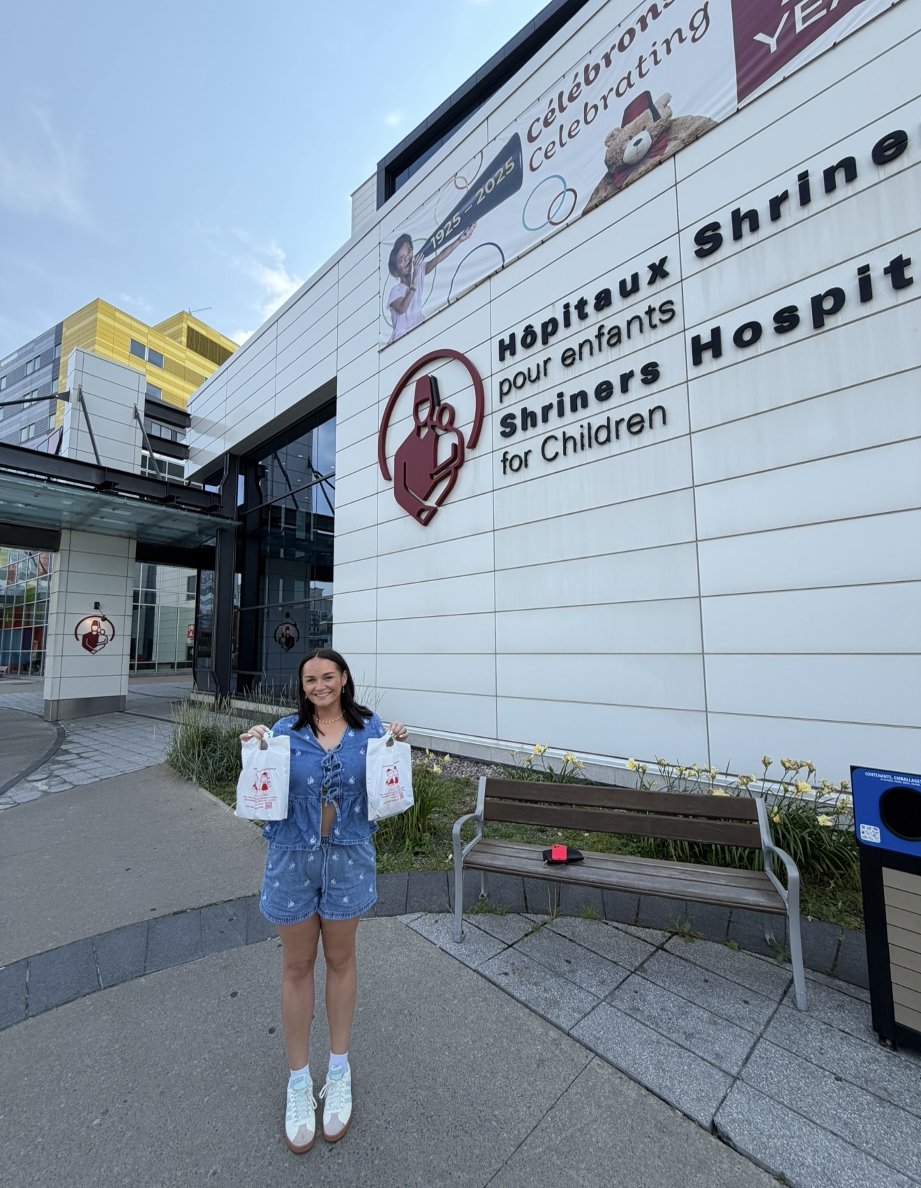 Young woman standing outside Shriner's Hospitals for Children building, smiling and holding two takeaway bags outside the entrance.