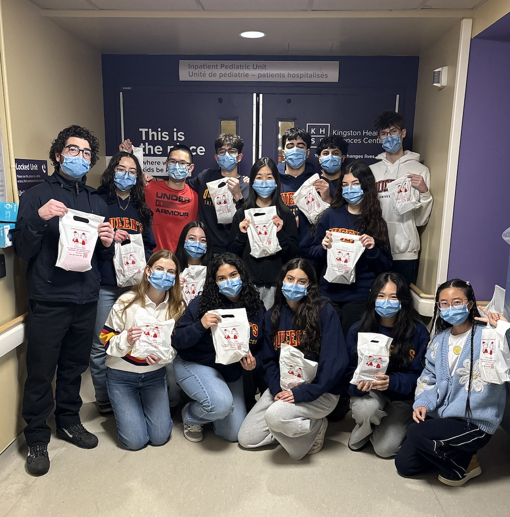 Group of students in masks in a hospital corridor, each holding a white bag with red graphics.