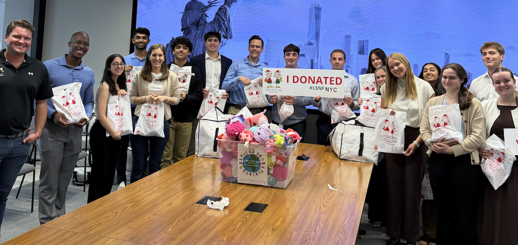 Group of people posing with donation bags and a sign that reads 'I DONATED' during a charity drive in a meeting room, with a toy-filled donation box on the table nearby.
